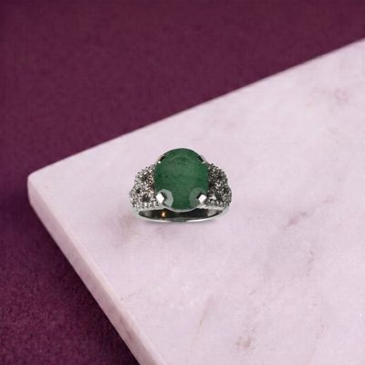 une bague sertie d'une émeraude et de diamants posée sur une dalle de marbre