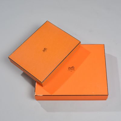 une boîte orange, dont le couvercle est ouvert, posée sur une surface blanche