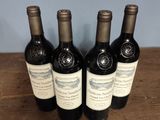 four bottles of wine are lined up on a wooden table