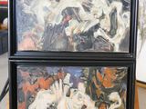 two paintings of horses are on display on a wooden table