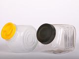 deux bocaux en plastique vides avec leurs couvercles, posés sur une surface blanche