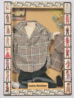 une poupée dans une boîte en carton, avec ses vêtements et ses accessoires exposés