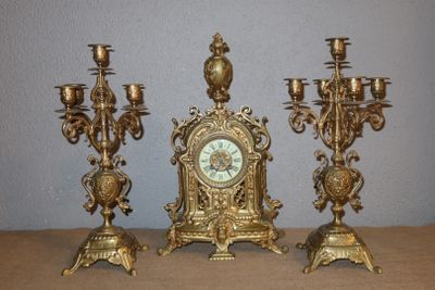 three gold colored candlesticks and a clock on a table