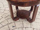 a wooden table with a round top sitting on a brick floor