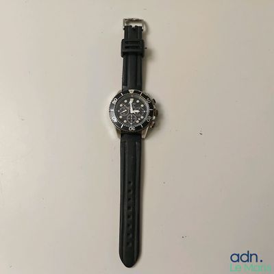 une photo d'une montre posée sur une surface blanche, avec un bracelet noir