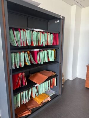 une bibliothèque sur laquelle sont posés de nombreux dossiers, dans une pièce