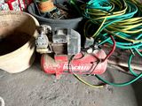 a small air compressor sitting on the floor next to a bucket of hoses