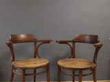 two wooden chairs with wicker seats against a gray wall