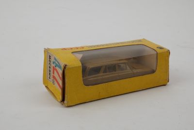 une petite voiture miniature dans une boîte jaune posée sur une surface blanche