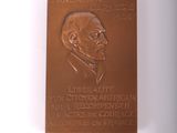 La plaque se trouve sur le mur d'un immeuble où est représenté un homme en costume-cravate.