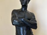 statue of a man standing with his arms crossed in front of a white wall