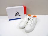white sneakers with orange laces on a white surface next to a box