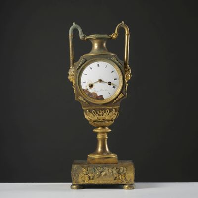 une horloge dorée posée sur un support, elle-même posé sur une table blanche