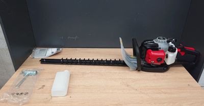une tondeuse rouge et noire posée sur une table à côté d'un outil