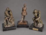 three bronze figurines of a man and woman sitting on a rock