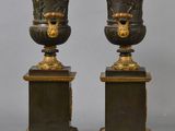 pair of antique bronze vases on pedestals on a gray background
