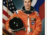 Un astronaute de la NASA en combinaison spatiale orange, tenant un casque et un drapeau américain