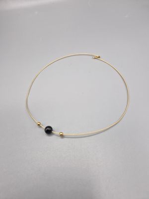 un collier plaqué or orné d'une perle noire sur un fond blanc