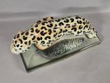 a figurine of a leopard laying on a glass base