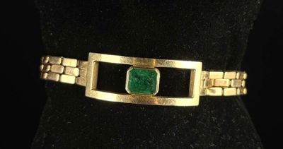 a close up of a gold bracelet with a green stone on it