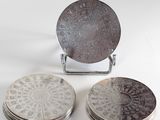 three silver plate coasters with designs on them sitting on a white surface