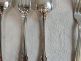 cinq cuillères en argent et deux cuillères en argent posées sur une nappe blanche