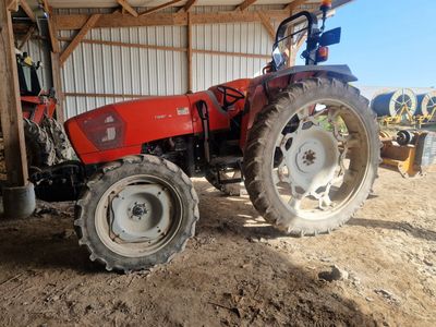 un tracteur rouge garé sur la terre battue