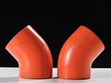 pair of orange pipe fittings on a white surface against a black background