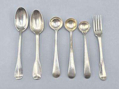 six cuillères en argent et une fourchette sont alignées sur une table