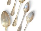 six silver spoons are arranged in a row on a white surface