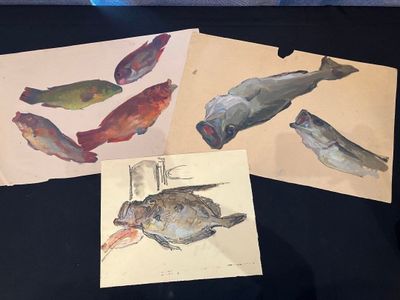 three paintings of fish on display on a table