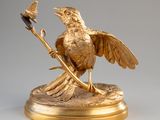 une statue en or représentant un oiseau sur une branche, sur laquelle est perché un autre oiseau