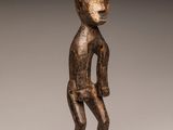 une statue en bois représentant un homme debout sur un socle noir