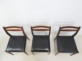 three chairs with black leather seats sit in front of a white wall