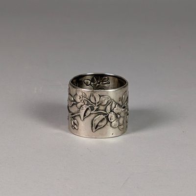 silver ring with flowers and leaves on it on a white surface