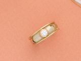 un gros plan d'une bague en or sertie d'un diamant, posée sur un fond rose