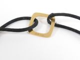 a close up of a black cord bracelet with a gold square on it