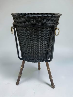 une jardinière en osier noir avec des poignées en laiton, posée sur un socle en bois