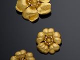 three gold flower brooches and a pair of earrings on a black surface