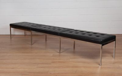 un banc noir posé sur un parquet, devant un mur blanc