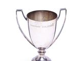 coupe de trophée plaquée argent posée sur un socle, sur fond blanc