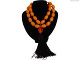 un collier de perles orange orné d'un pompon noir, posé sur un mannequin