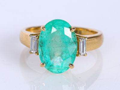 une bague ovale sertie d'une émeraude et de diamants, agrémentée de diamants taille baguette sur un fond blanc