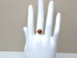 a hand with a ring on it that has a red stone on it