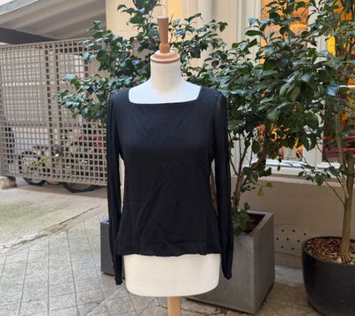 un haut noir à manches longues posé sur un mannequin devant un arbre en pot