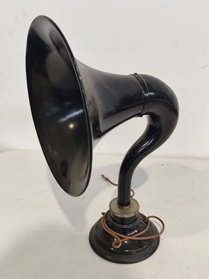 un vieux gramophone noir posé sur un support, devant un fond blanc