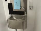 un lavabo en inox dans une salle de bains, avec une pancarte bleue accrochée au mur