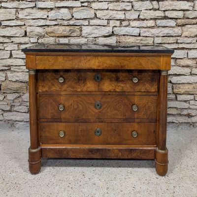 an antique chest of drawers with marble top in front of a stone wall