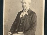 une vieille photo représentant un homme en costume-cravate, assis sur une chaise