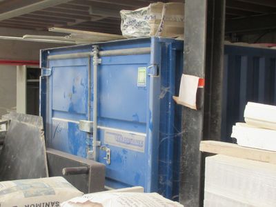 une benne bleue posée dans un entrepôt rempli de cartons